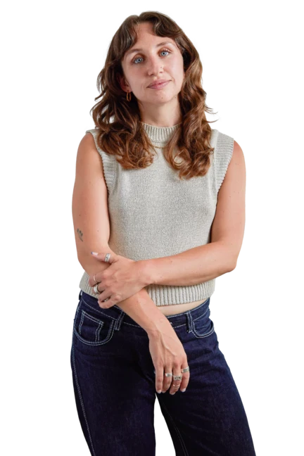 Louise is wearing black trousers and a black cardigan as she sits on a wooden stool and looks directly into the camera with an expression of quiet confidence.